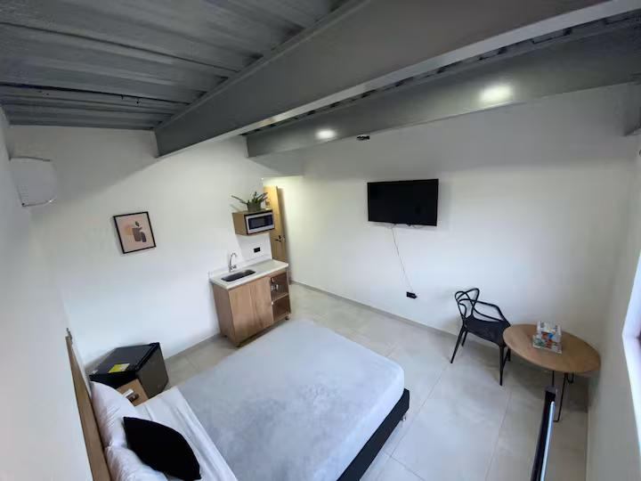 Vista amplia del estudio con cama doble, escritorio y televisión en Medellín