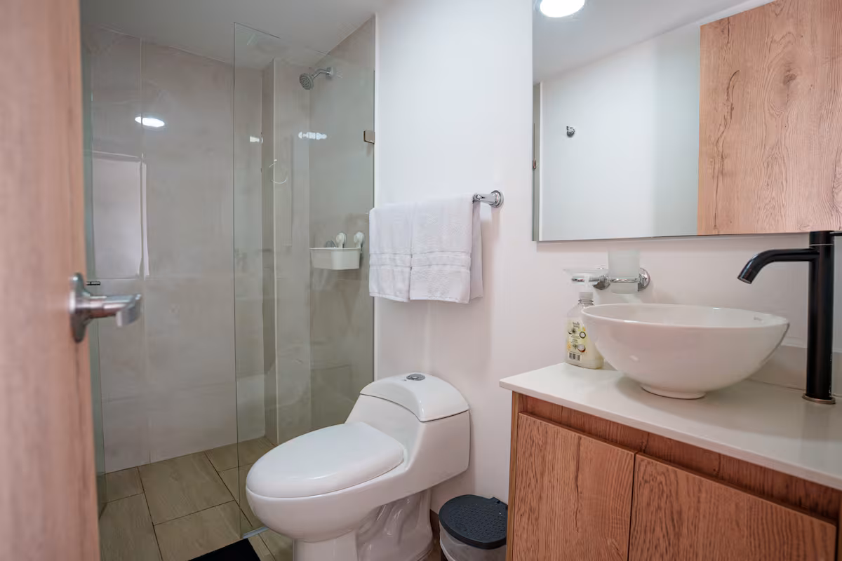 Baño privado moderno con ducha de vidrio, lavabo sobrepuesto y acabados en madera